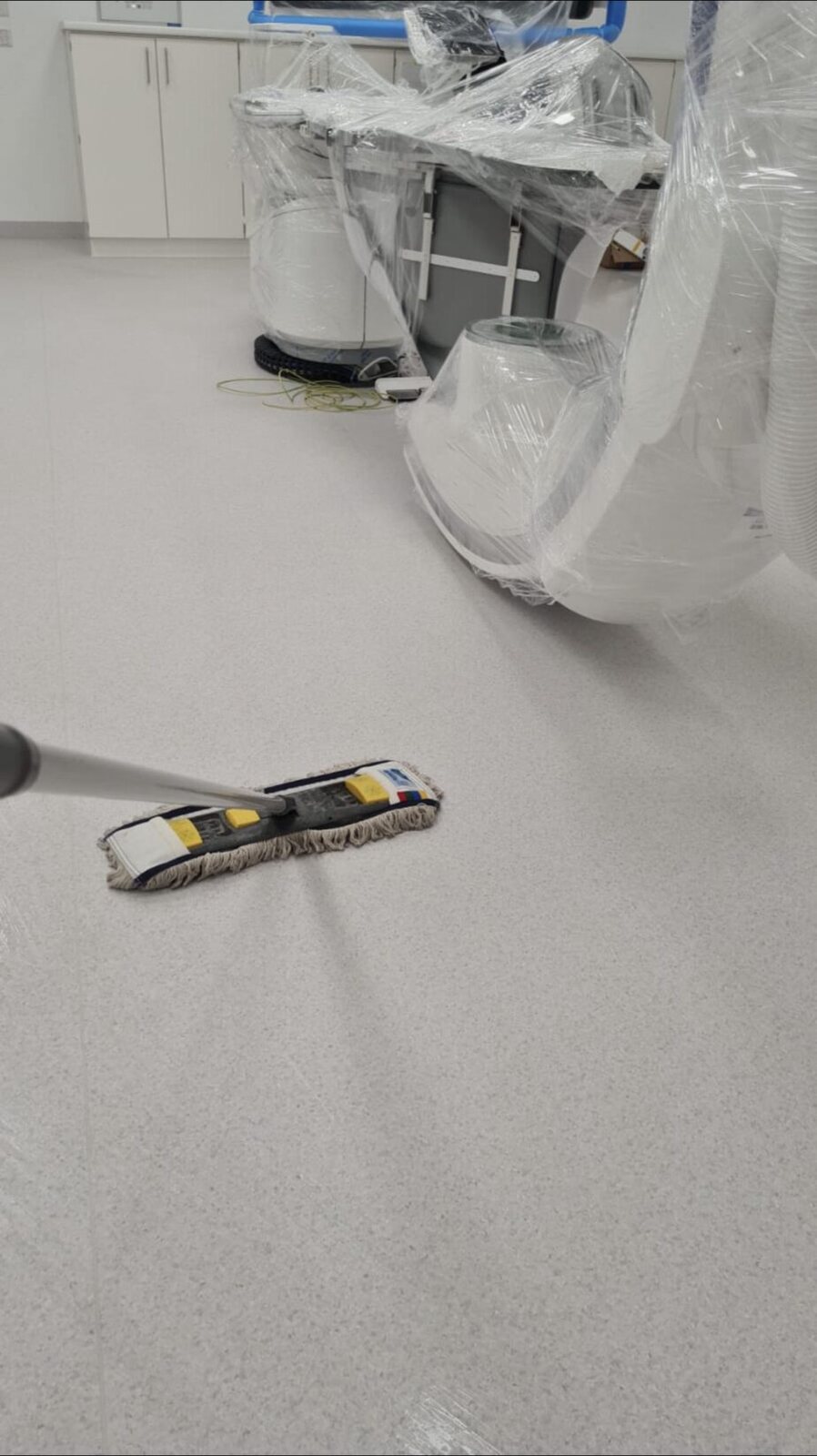 Flachmopp auf hellem Boden neben mit Schutzfolie abgedeckten Geräten