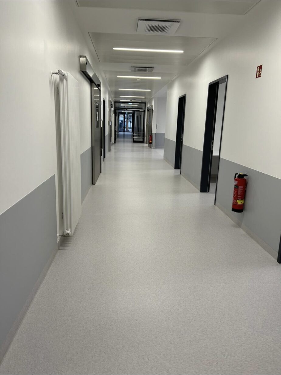 Freier Krankenhausflur mit gleichmäßig hellem Boden und grauen Wandsockeln