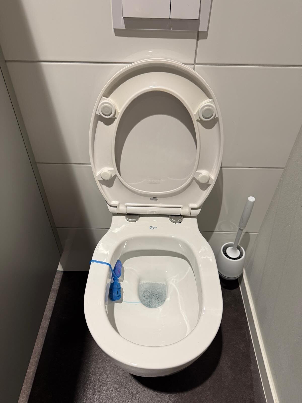 Weiße Toilette mit hochgeklapptem Sitz und blauem WC-Einhänger