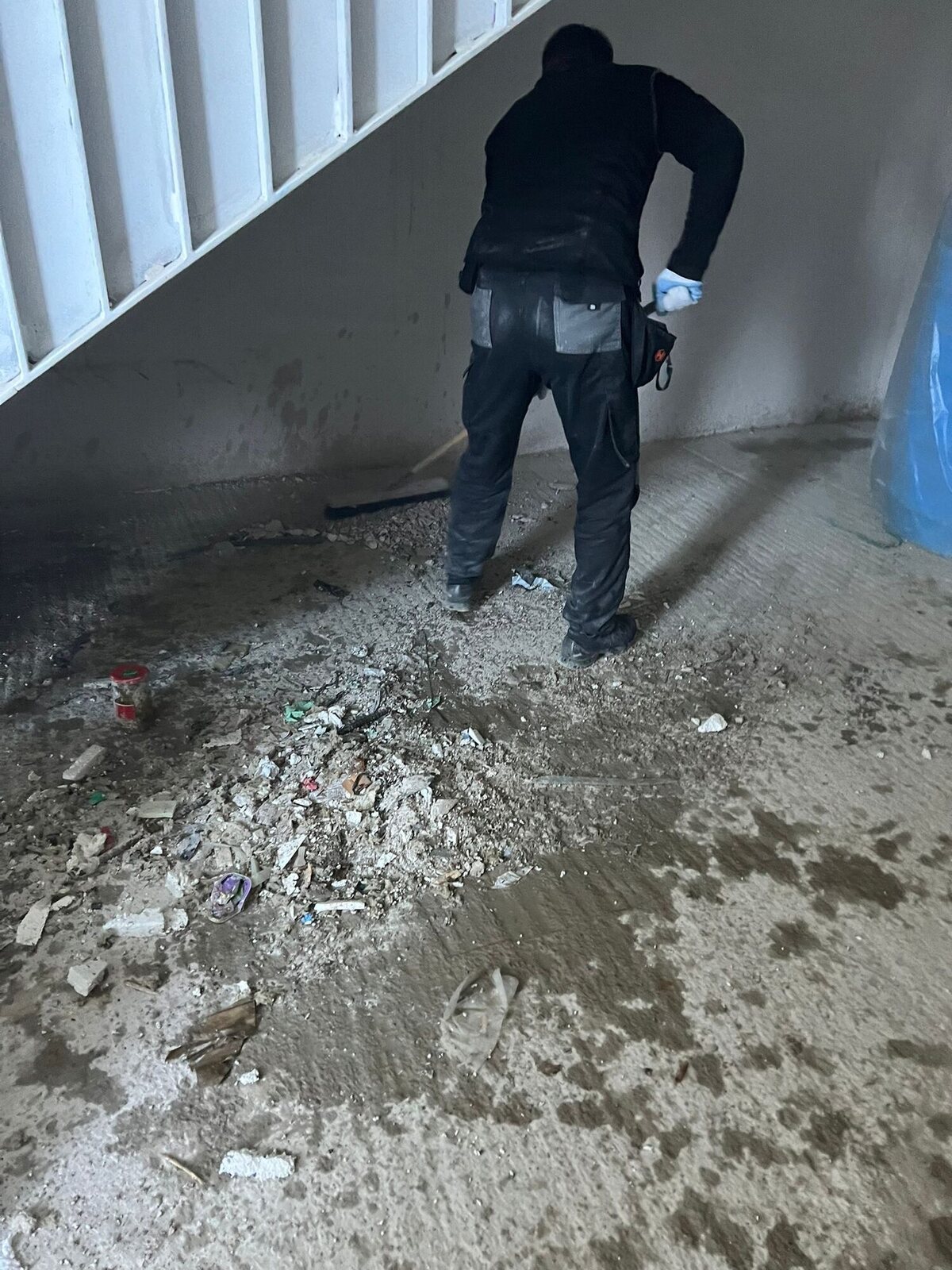 Mitarbeiter beim Zusammenkehren loser Baureste unter einer Treppe