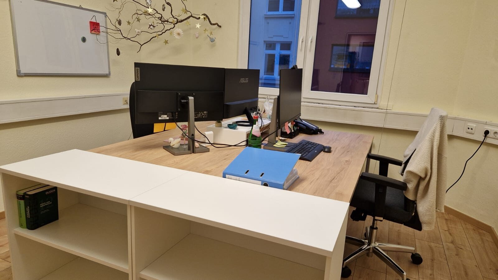 Eingerichtetes Büro mit belegten Schreibtischen und offenen weißen Regalen