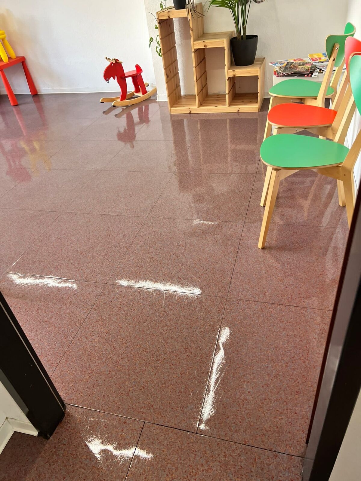 Glänzender rötlicher Boden im Wartebereich mit bunten Stühlen und Schaukelpferd