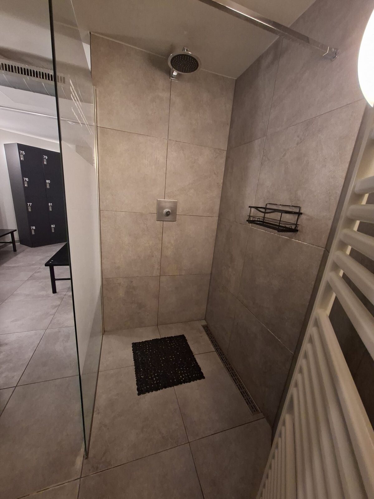Dusche mit grauen Wandfliesen, schwarzer Bodenmatte und wandnaher Ablaufrinne