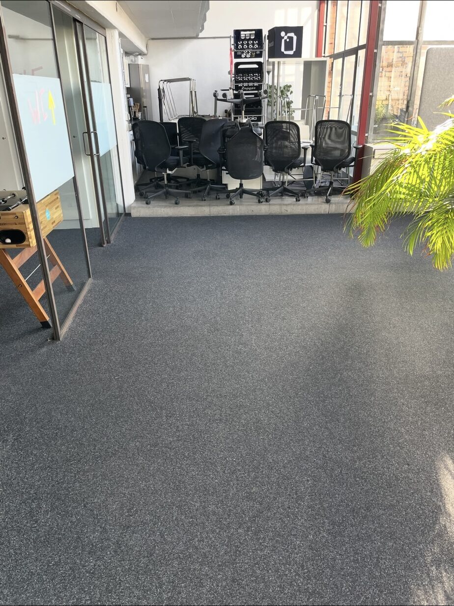Freie Teppichfläche vor zusammengestellten Bürostühlen neben einer Glaswand