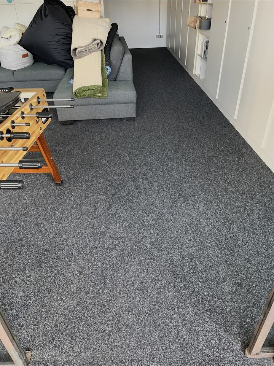 Grau melierter Teppichboden zwischen beladenem Sofa und weißen Schränken