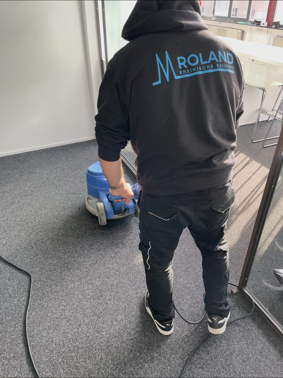 Mitarbeiter führt eine blaue Einscheibenmaschine über grauen Teppichboden im Büro