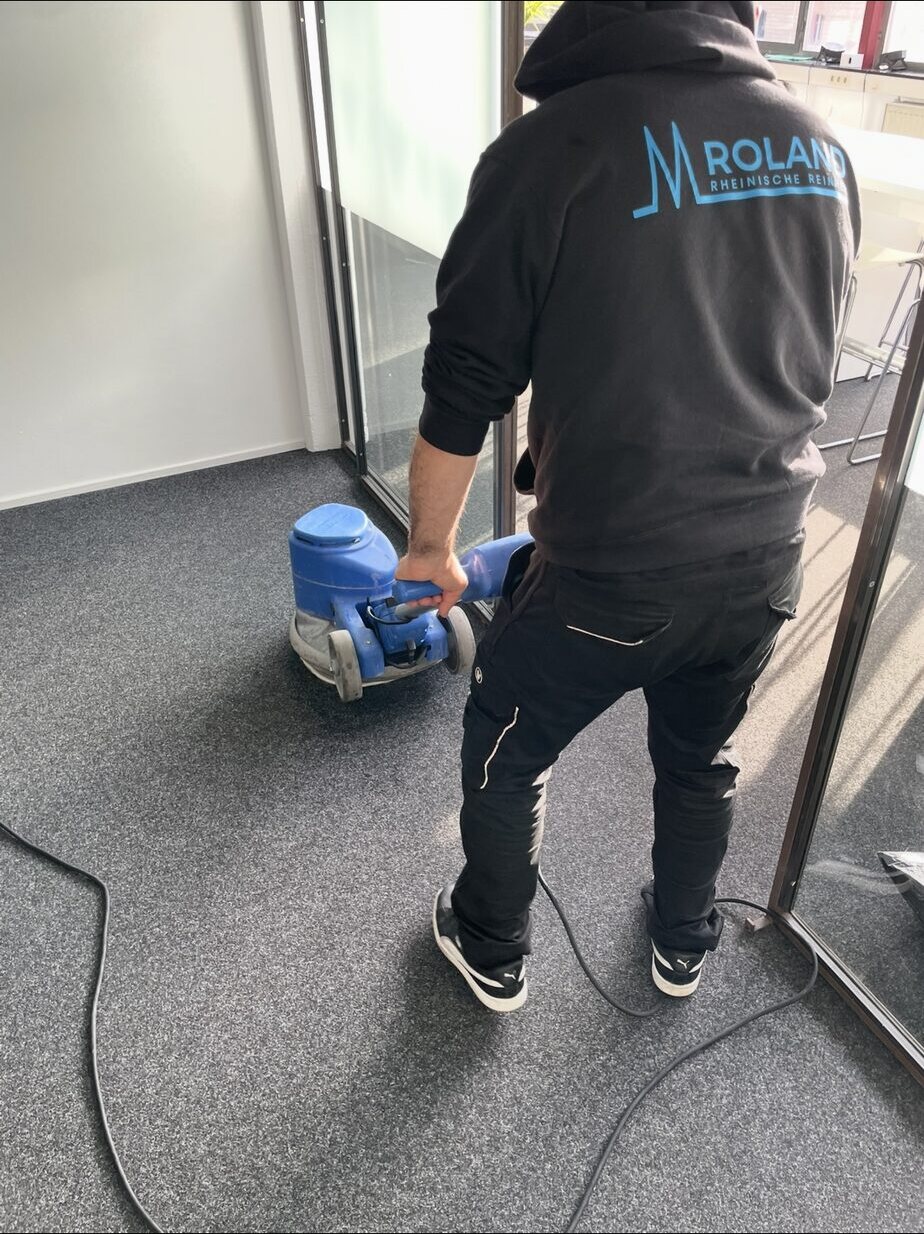 Teppichboden vor einer Glastrennwand wird mit einer Einscheibenmaschine behandelt