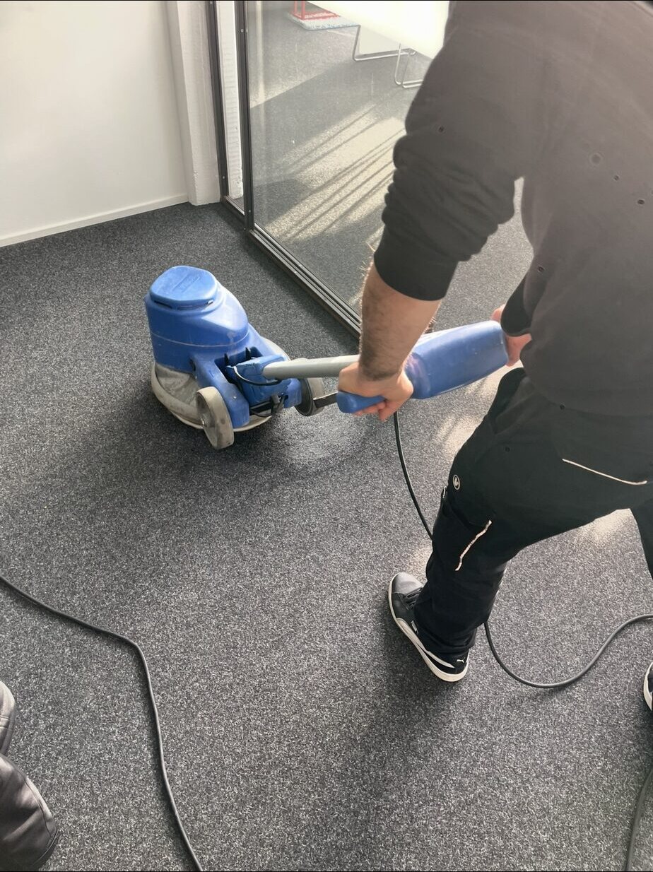 Mitarbeiter hält die Einscheibenmaschine mit beiden Händen auf dem grauen Teppich