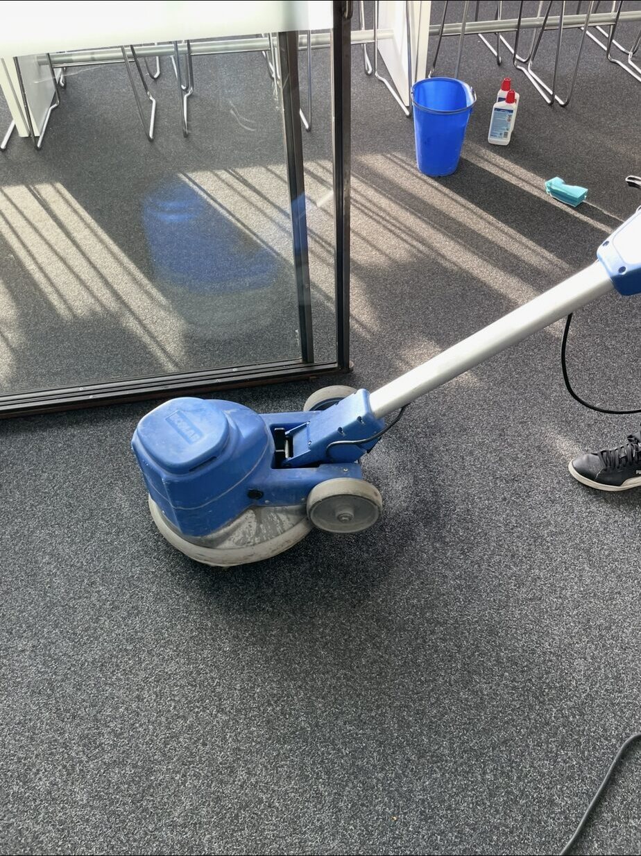 Abgesenkter Maschinenkopf auf grauem Büroteppich mit Eimer im Hintergrund