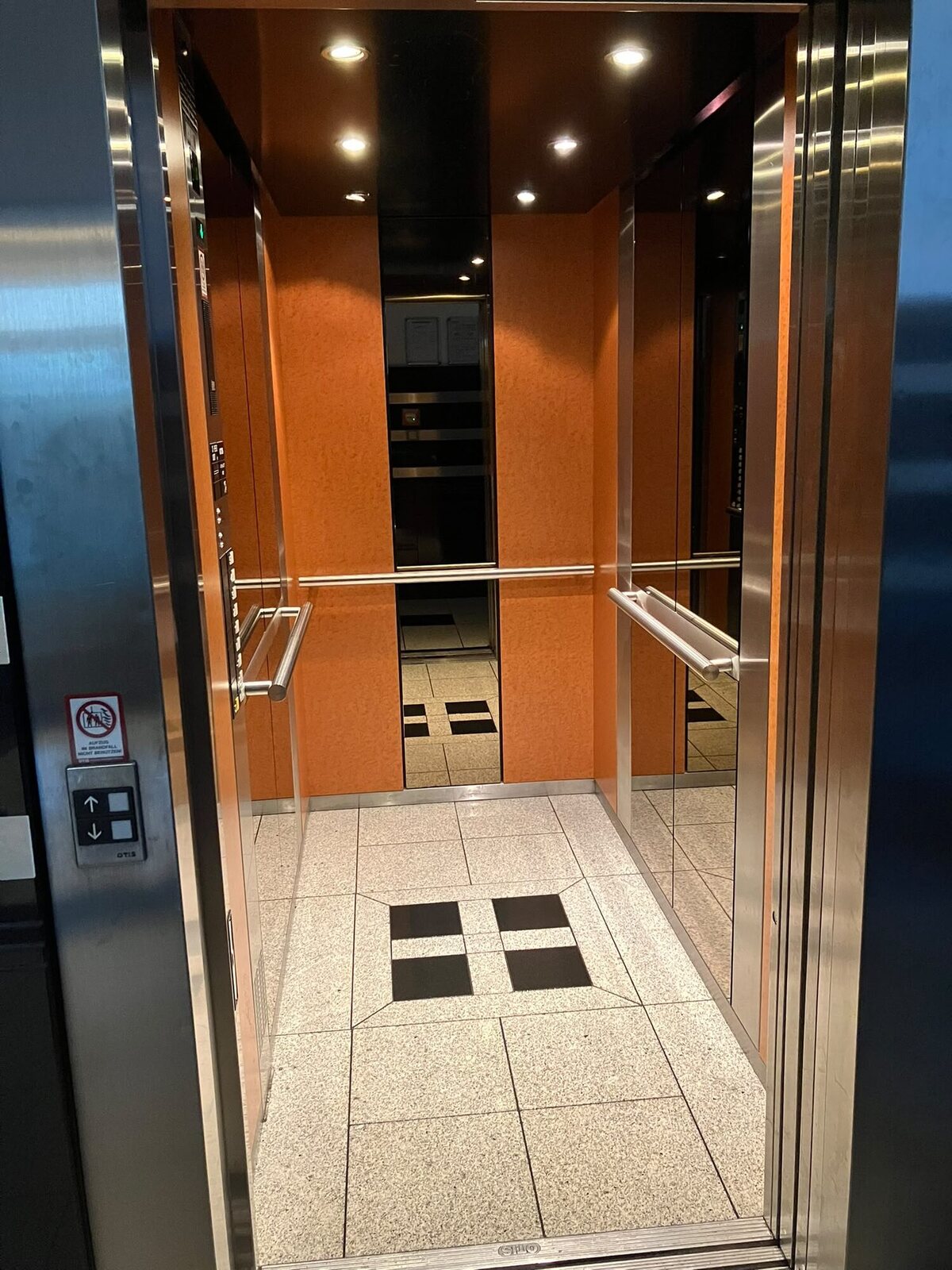 Aufzugkabine mit sauberem Fliesenboden und Spiegeln zwischen orangefarbenen Wandverkleidungen
