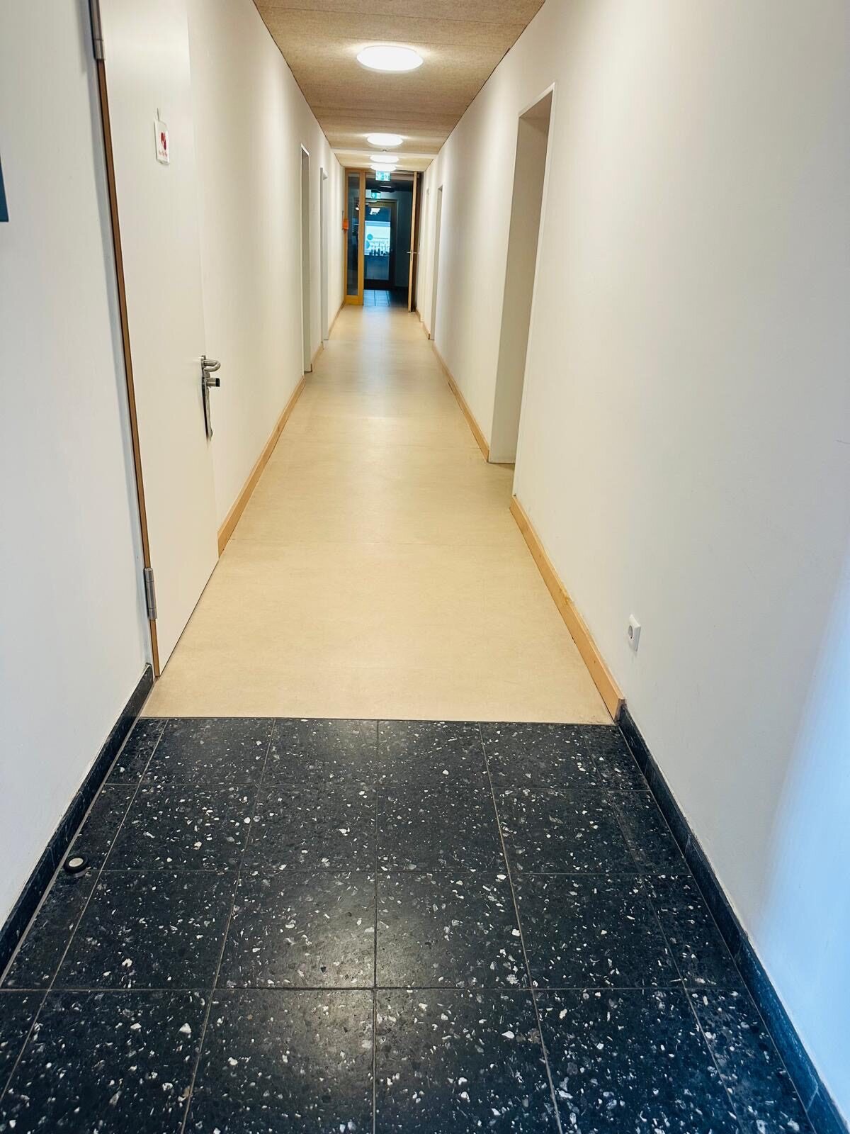 Flur mit fleckenfrei wirkendem hellem Bodenbelag und dunklen gesprenkelten Fliesen